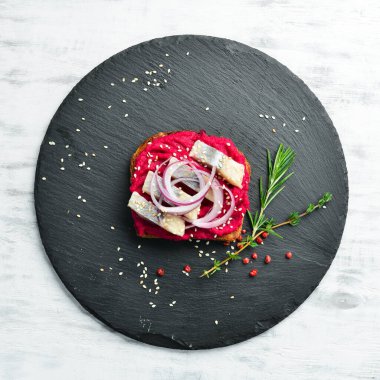 Pancar humusu, ringa balığı ve soğanlı sandviç. Kahvaltıda. Siyah taştan bir tabakta.