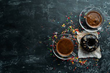 Siyah taş bir masanın üzerinde bir fincan kahveyle çikolatalı tatlı çörek. Üst görünüm.