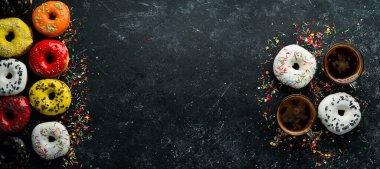 Siyah taş bir masanın üzerinde bir fincan kahveyle bir dizi tatlı renkli çörek. Üst Manzara. Düz Yat.