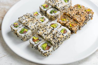 Geleneksel suşi ruloları ve susamlı maki, avokado ve balık. Japon yemeği. Üst Manzara. Beyaz bir arkaplanda.