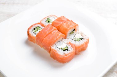 Suşi, avokado ve somonla birlikte beyaz tabakta yuvarlanıyor. Üst Manzara. Beyaz bir arkaplanda.