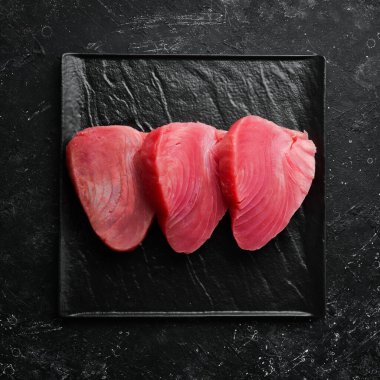 Siyah bir tabakta taze sulu ton balığı bifteği. Karanlık bir arka planda. Üst görünüm.