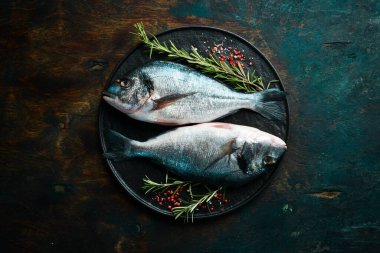 Siyah taş tabakta baharatlı iki dorado balığı. Karanlık bir arka planda. Üst görünüm.