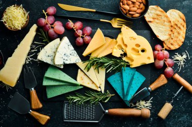 Büyük bir peynir seti, fındık, üzüm ve atıştırmalık siyah taş arka planda. Bedava fotokopi. Üst görünüm.