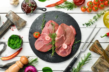 - Et. Biberiye ve baharatlı çiğ kemiksiz kuzu bifteği. Beyaz ahşap bir arka planda. Üst görünüm.