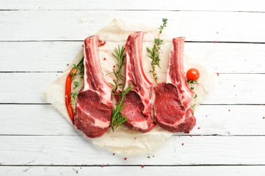Kemiğin üzerinde çiğ biftek, biberiye ve baharatla. Beyaz ahşap bir arka planda. Üst görünüm.