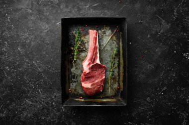 Kemiğin üzerinde taze çiğ biftek ve biberiye ve baharat. Siyah taştan bir arka planda. Üst görünüm.
