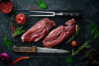 Çiğ ördek göğsü, taze sebzeler ve baharatlarla kesme tahtasına yakın çekim. Siyah bir arka planda. Üst görünüm.