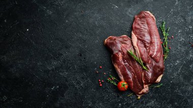 Çiğ ördek göğsü, taze sebzeler ve baharatlarla kesme tahtasına yakın çekim. Siyah bir arka planda. Üst görünüm.