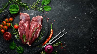 Çiğ ördek göğsü, taze sebzeler ve baharatlarla kesme tahtasına yakın çekim. Siyah bir arka planda. Üst görünüm.