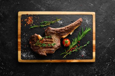 Kemiğe baharatlı dana biftek, kekik ve biberiye. Üst Manzara. Siyah taş kesme masasının üstünde düz bir görünüm vardı..