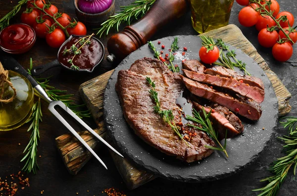 Baharatlı sulu dana biftek, kekik ve biberiye. Üst Manzara. Siyah taş kesme masasının üstünde düz bir görünüm vardı..