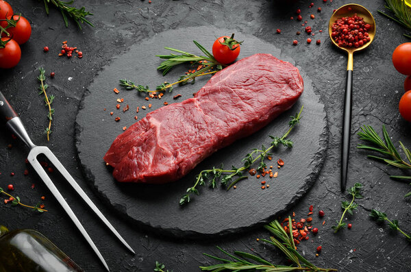 Raw sirloin steak with thyme, rosemary and spices. Top view. Flat lay top view on black stone cutting table.