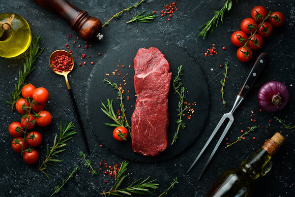 Raw sirloin steak with thyme, rosemary and spices. Top view. Flat lay top view on black stone cutting table.