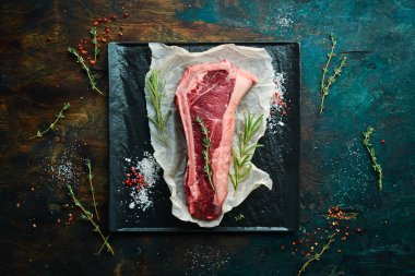 Kemiğin üzerinde çiğ biftek, kekik, biberiye ve baharatla birlikte. Üst Manzara. Siyah taş kesme masasının üstünde düz bir görünüm vardı..