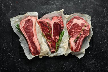 - Et. Çiğ biftek seti - T-bone, tomahawk, striploin, fileto, New York bifteği. Siyah taş kesme masasının üstünde düz bir görünüm vardı..