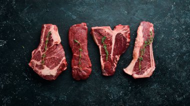 Çiğ biftek seti - T-bone, tomahawk, striploin, fileto, New York bifteği. Siyah taştan bir arka planda. Üst görünüm.