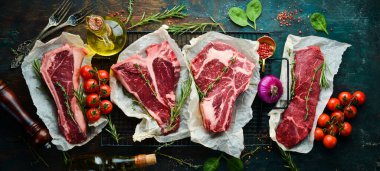 Çiğ biftek seti - T-bone, tomahawk, striploin, fileto, New York bifteği. Siyah taştan bir arka planda. Üst görünüm.