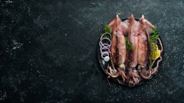 Siyah taş tabakta çiğ deniz mürekkep balığı pişmeye hazır. Üst Manzara. Karanlık bir arka planda.