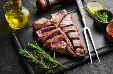 Yıllanmış biftek T-Bone bifteği. Biberiye ve baharatlı sulu biftek. Üst Manzara. Kırsal tarzda. Düz Yat.