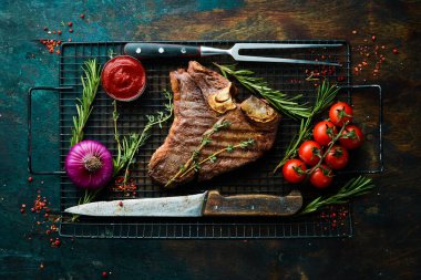 Yıllanmış biftek T-Bone bifteği. Biberiye ve baharatlı sulu biftek. Üst Manzara. Kırsal tarzda. Düz Yat.