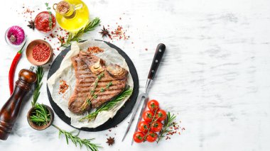 Yıllanmış biftek T-Bone bifteği. Biberiye ve baharatlı sulu biftek. Üst Manzara. Kırsal tarzda. Düz Yat.