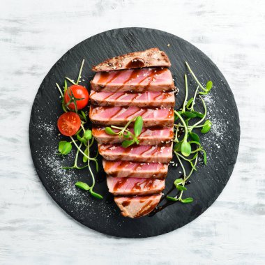 Siyah taş tabakta sebzeli sulu ton balığı bifteği pişirdim. Restoran yemeği. Deniz ürünleri. Kırsal tarzda. Düz Yat.