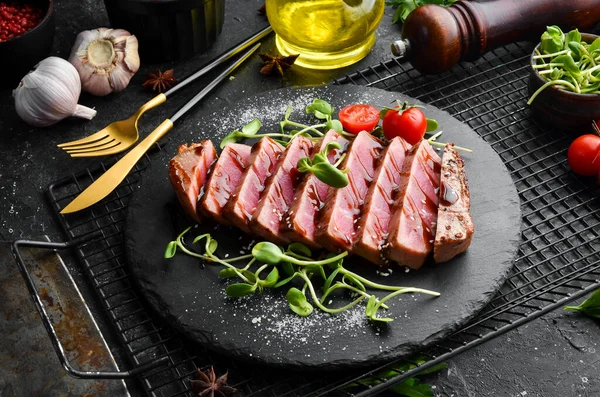 Cooked juicy tuna steak with vegetables on a black stone plate. Restaurant food. Seafood. Rustic style. Flat Lay.