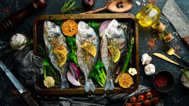 Metal tepside sebzeli çiğ Dorado balığı. Balık pişirme tarifi. Üst Manzara. Bedava fotokopi. Siyah taştan bir arka planda.