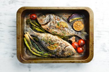 Lezzetli fırında pişirilmiş, otlu ve limonlu balık, metal fırın tepsisinde. Dorado. Beyaz ahşap arka planda.