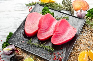 Siyah taştan bir tabakta taze ton balığı bifteği. Beyaz ahşap bir arka planda. Üst görünüm.