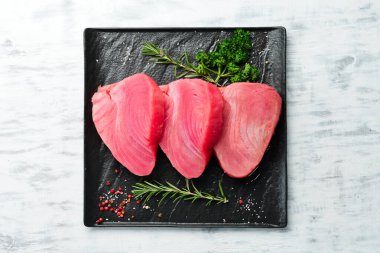 Siyah taştan bir tabakta taze ton balığı bifteği. Beyaz ahşap bir arka planda. Üst görünüm.