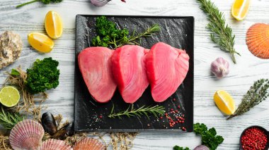 Siyah taştan bir tabakta taze ton balığı bifteği. Beyaz ahşap bir arka planda. Üst görünüm.