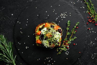 Sandviç: ciabatta, avokado, pancar ve havuç. Kahvaltıda. Siyah taştan bir tabakta.