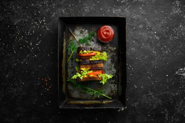 Siyah taşlı arka planda sosisli, soğanlı, peynirli ve marullu ev yapımı sandviç. Kırsal tarzda. Boş kopyalama alanı.