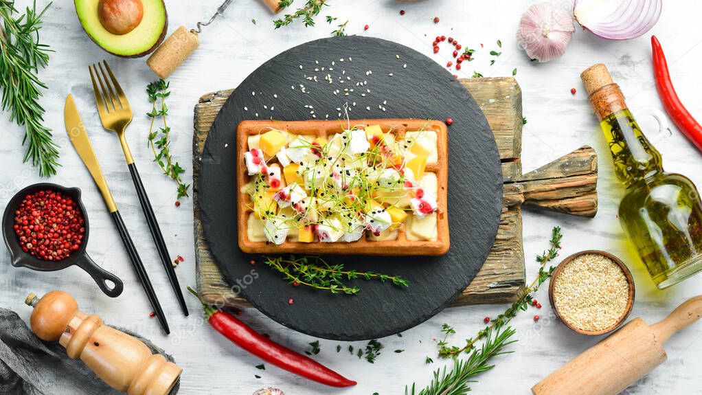 Breakfast. Belgian waffles with brie cheese, feta and parmesan. On a black stone plate.