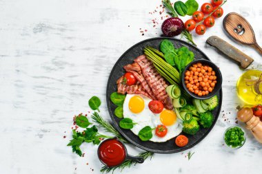 İngiliz kahvaltısı: nohut, avokado, çırpılmış yumurta, siyah taş tabakta domuz pastırması sebzesi. Üst Manzara. Metin için boş alan.