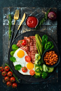 İngiliz kahvaltısı: nohut, avokado, çırpılmış yumurta, siyah taş tabakta domuz pastırması sebzesi. Üst Manzara. Metin için boş alan.
