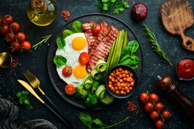 İngiliz kahvaltısı: nohut, avokado, çırpılmış yumurta, siyah taş tabakta domuz pastırması sebzesi. Üst Manzara. Metin için boş alan.