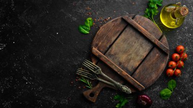 Mutfak tahtası, sebzeler, baharatlar ve otlar siyah taştan bir arka planda. Mutfak arka planı. Üst Manzara. Metin için boş alan.