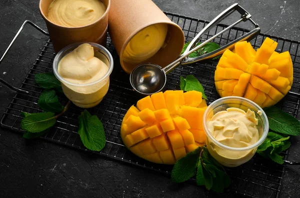 Mango ice cream with mint and fresh mango. Ice cream spoon. On a black stone background, top view.