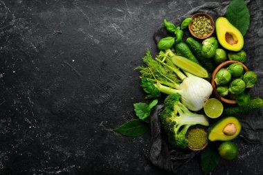 Taze yeşil sebze ve baharatlar: rezene, avokado, salatalık, limon, lahana ve fesleğen. Organik sağlıklı vejetaryen yemekleri. Siyah taştan bir arka planda.