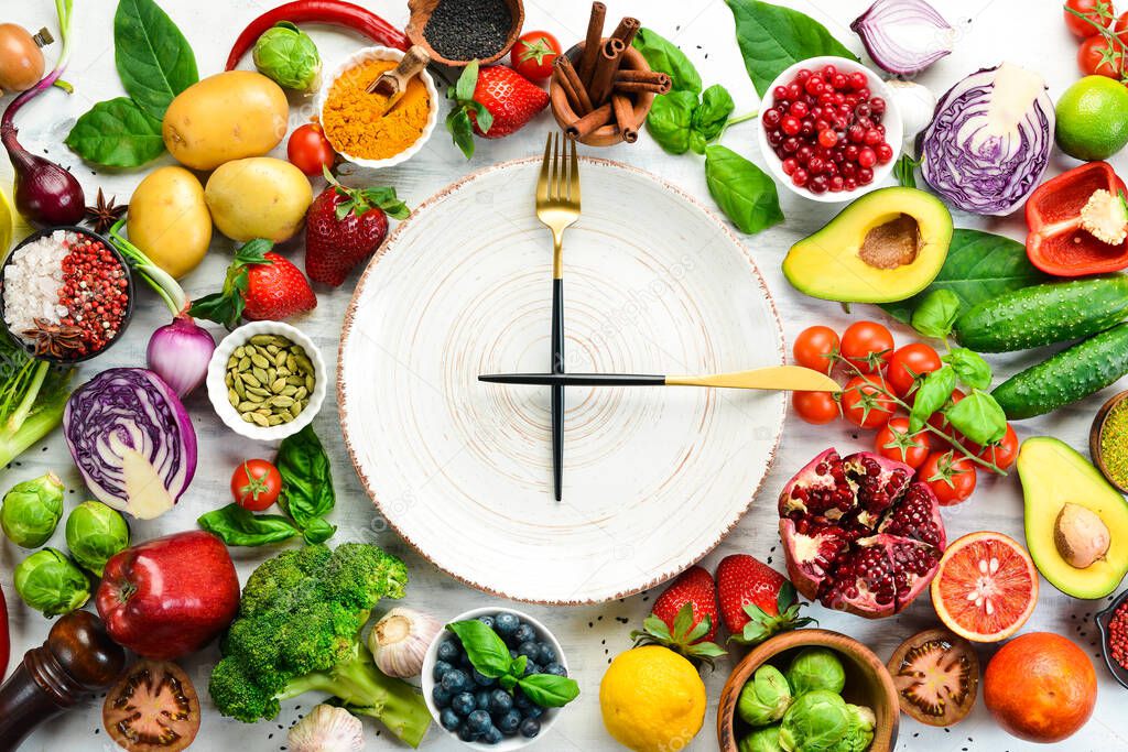 The concept of dietary nutrition: fresh vegetables and fruits. Cutlery and a plate in the form of a clock. Top view. Free space for your text.