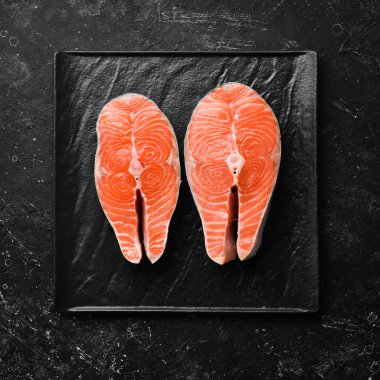 Siyah taş tabakta biberiyeli iki çiğ somon bifteği. Karanlık bir arka planda. Üst görünüm.