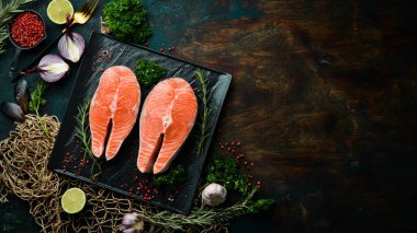 Siyah taş tabakta biberiyeli iki çiğ somon bifteği. Karanlık bir arka planda. Üst görünüm.