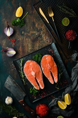 Siyah taş tabakta biberiyeli iki çiğ somon bifteği. Karanlık bir arka planda. Üst görünüm.