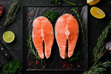 Siyah taş tabakta biberiyeli iki çiğ somon bifteği. Karanlık bir arka planda. Üst görünüm.