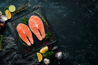 Siyah taş tabakta biberiyeli iki çiğ somon bifteği. Karanlık bir arka planda. Üst görünüm.