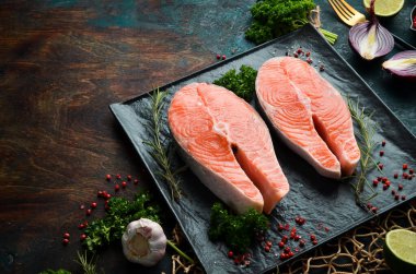 Siyah taş tabakta biberiyeli iki çiğ somon bifteği. Karanlık bir arka planda. Üst görünüm.