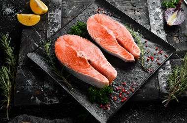 Siyah taş tabakta biberiyeli iki çiğ somon bifteği. Karanlık bir arka planda. Üst görünüm.